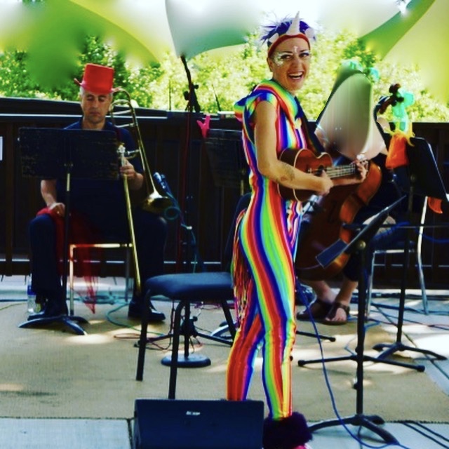 Jenifer in rainbow costume performing with musicians at Britt Music & Arts Festival